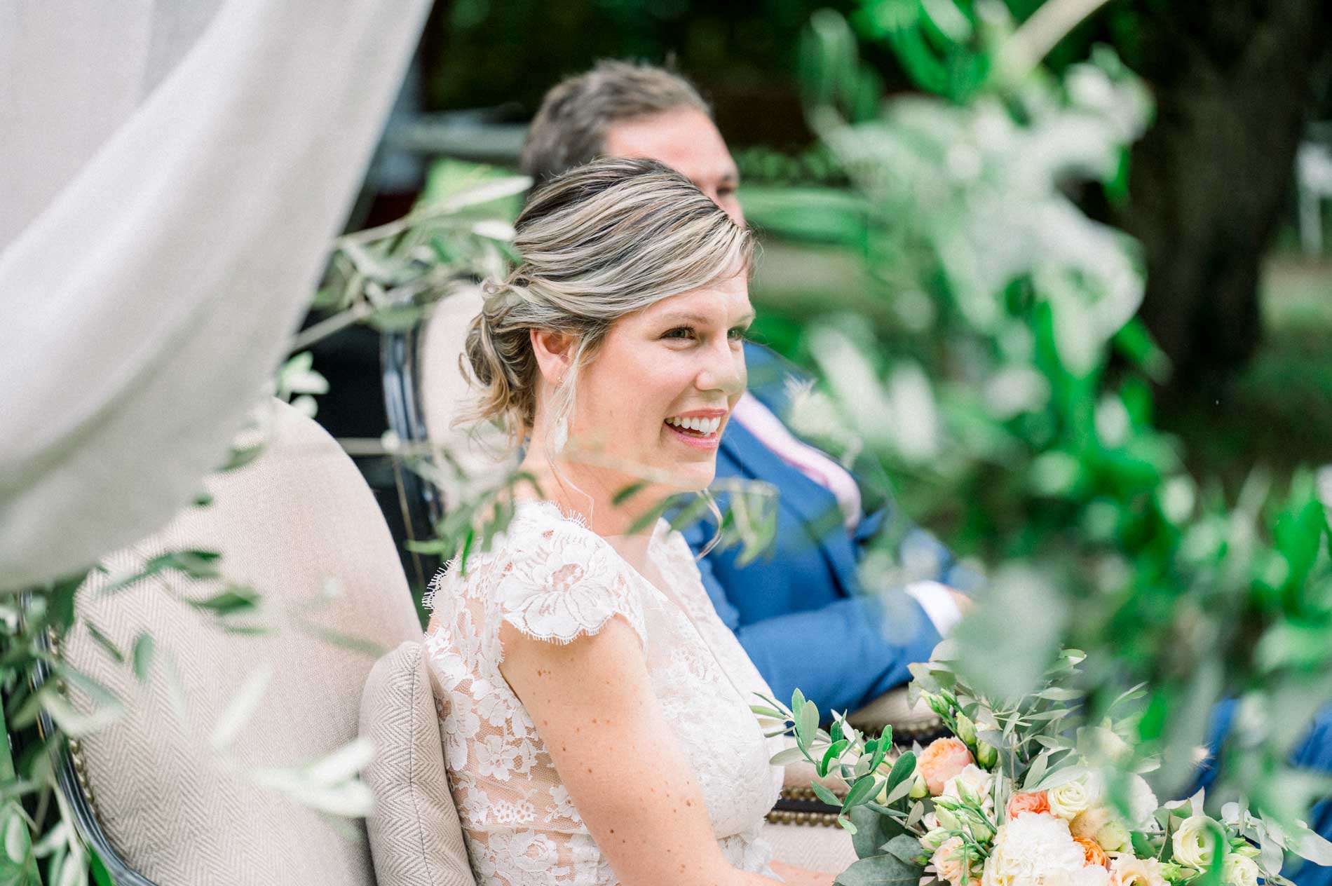 Bride smiling during the ceremony, framed by foliage and draped fabric