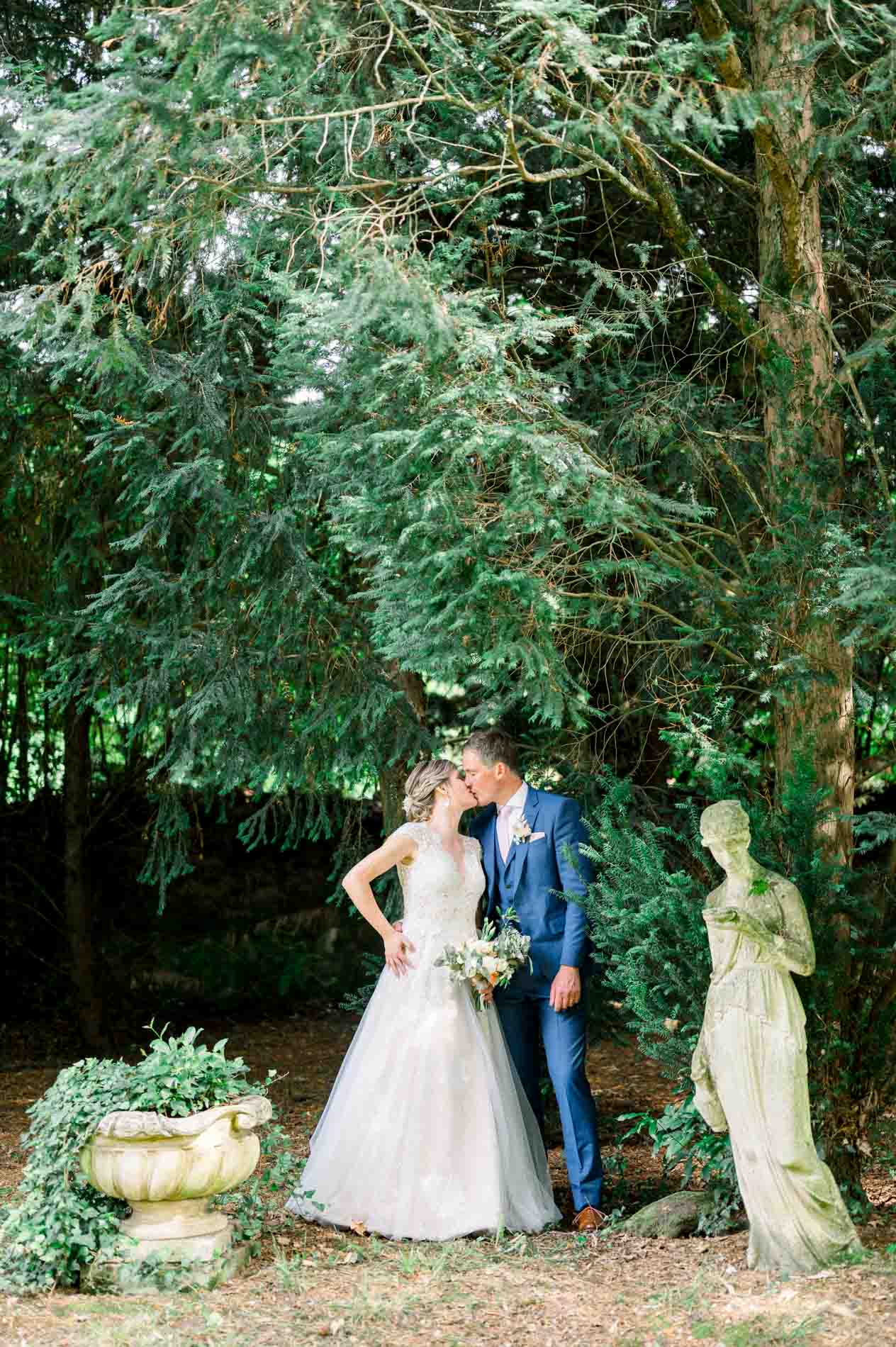 Bride and groom kissing beside a statue and flower urn in the grounds