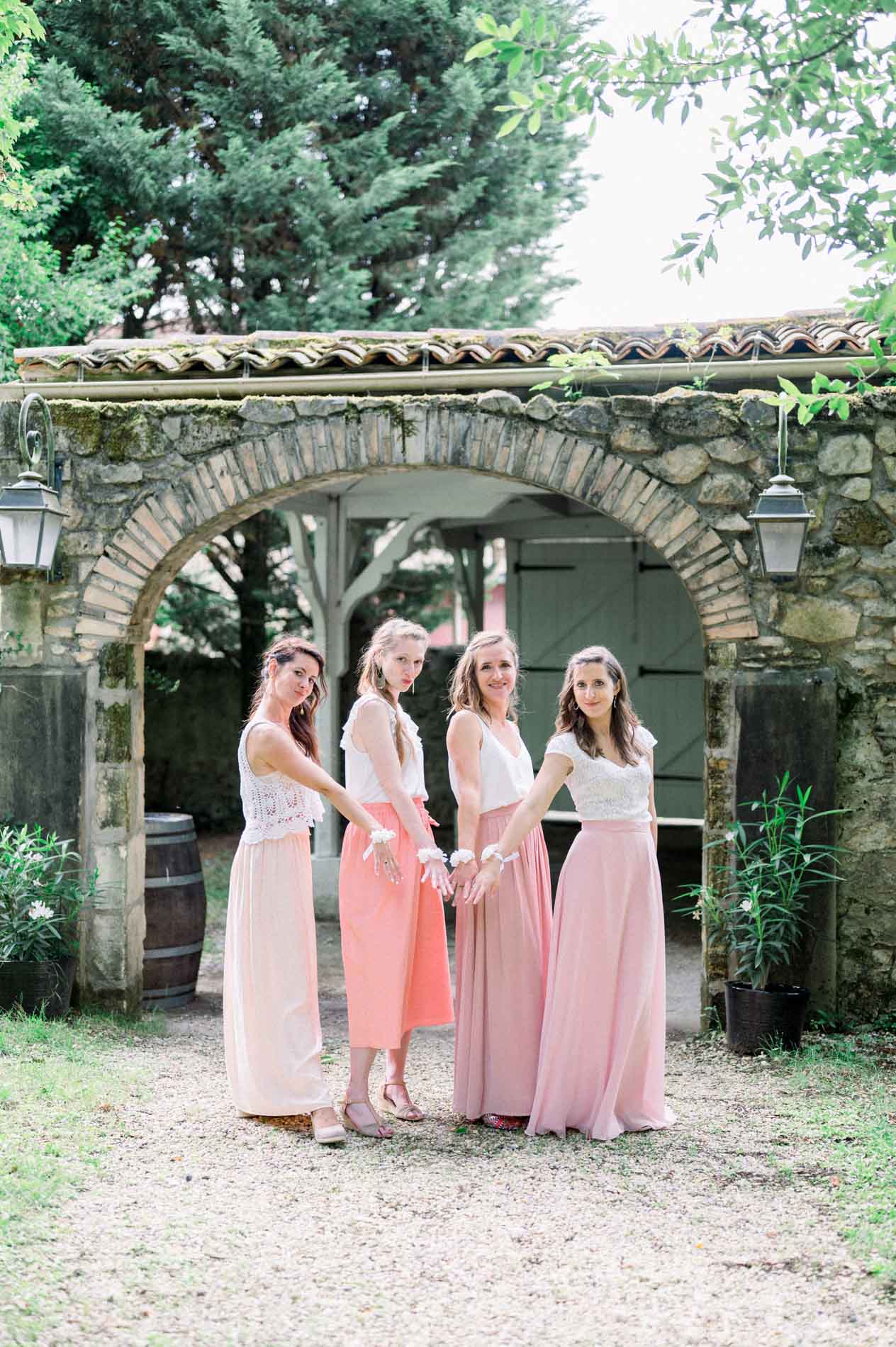 Bridesmaids in pink skirts beneath the stone archway at the Chartreuse