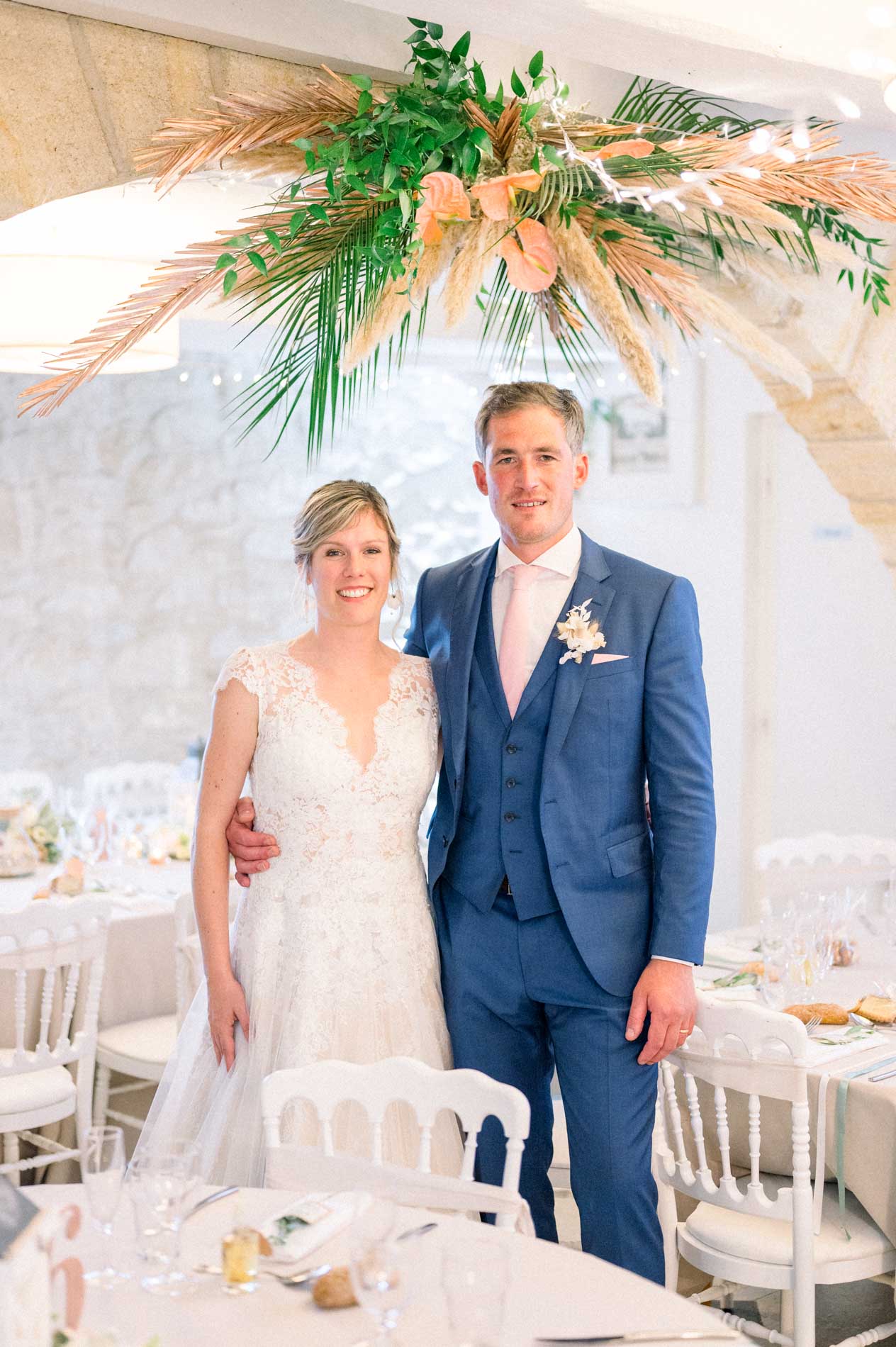 Bride and groom beneath a hanging pampas and dried palm installation