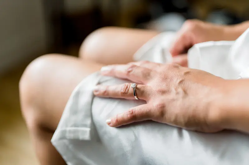 Hands of a loved one resting on white fabric, wedding ring on her finger