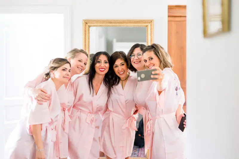 Bride and friends in pink robes taking a selfie while getting ready