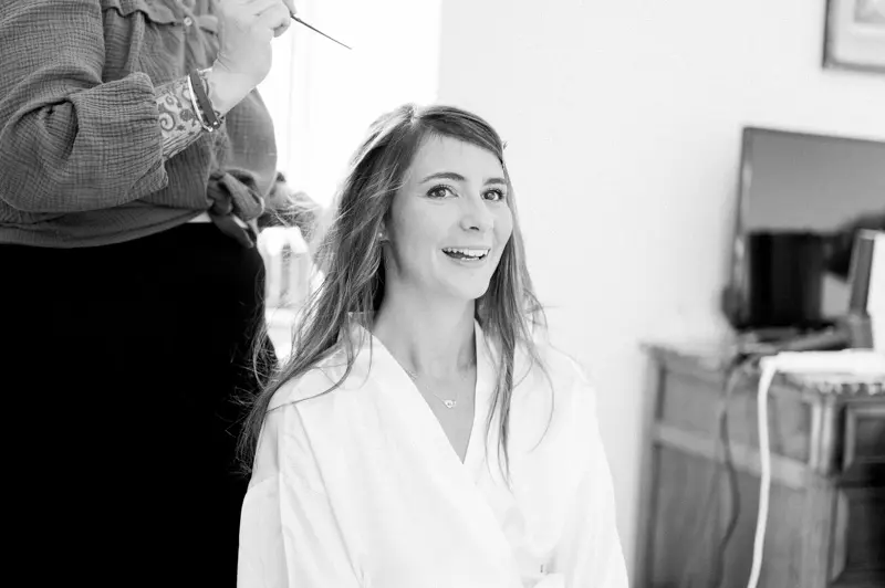 Smiling bride in a white robe having her hair done, black and white