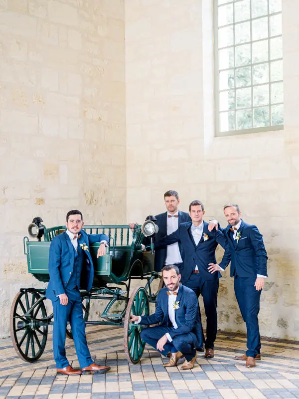 Groom and groomsmen in blue suits around an antique carriage