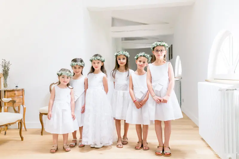 Five little flower girls in white dresses lined up in a bright room