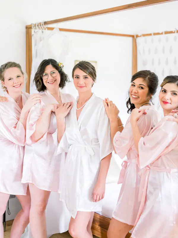 Bridesmaids in pink robes posing playfully by the four-poster bed