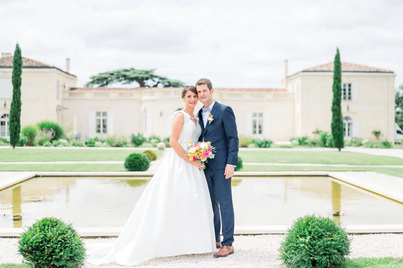 Bride and groom side by side by the pool in front of Château Gassies