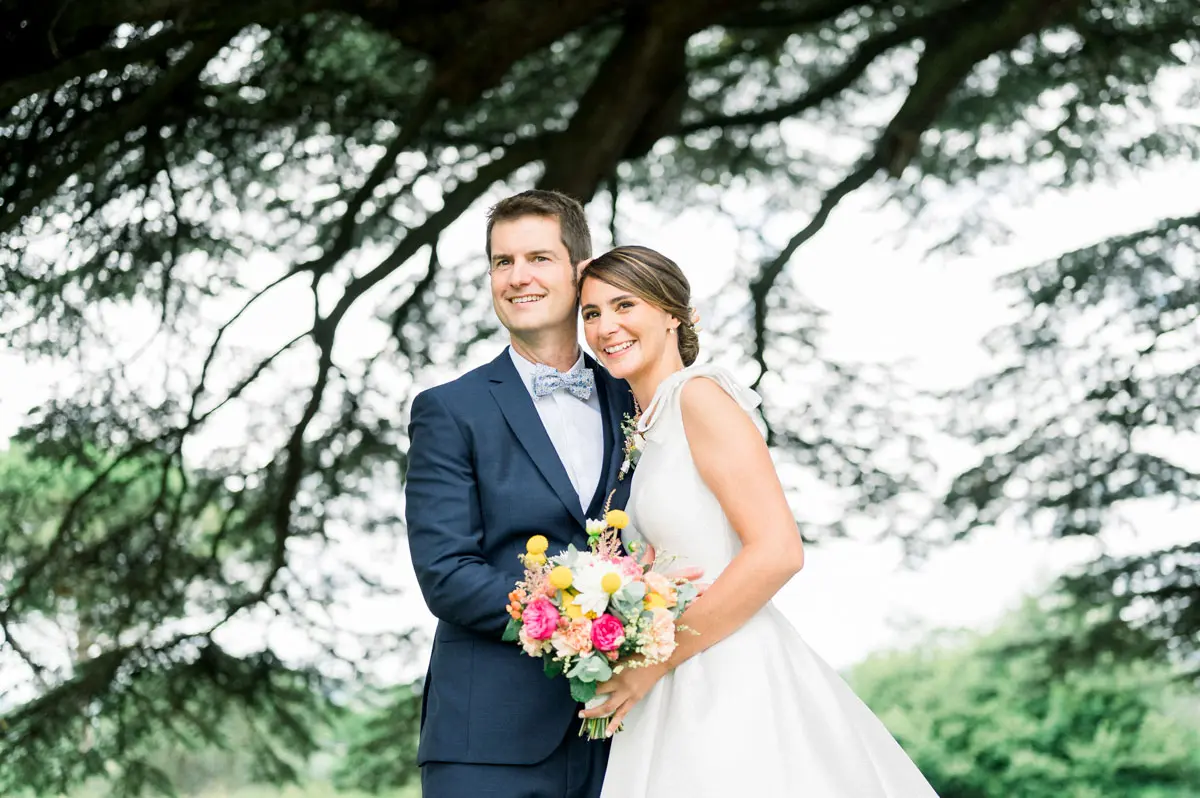Smiling couple beneath the cedar branches, colourful bouquet in hand