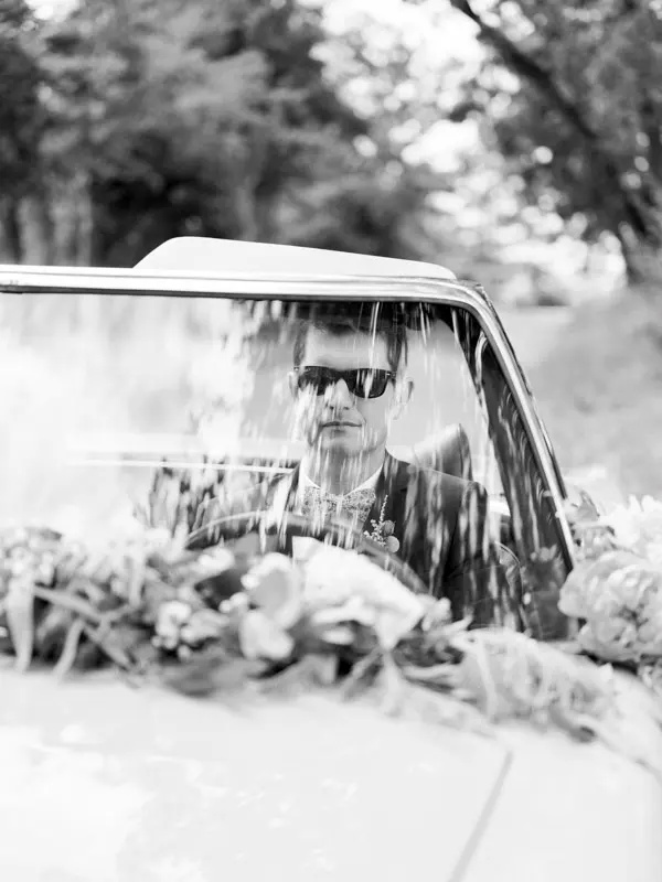 Driver in sunglasses at the wheel of the flower-decked convertible, black and white