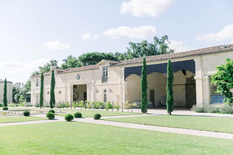 Lawn and stone outbuildings of Château Gassies under a summer sky
