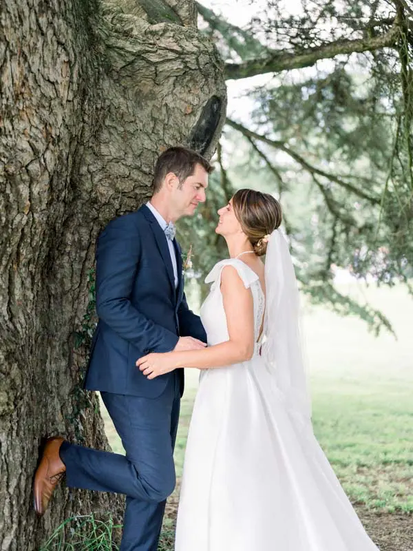 Groom leaning against the cedar trunk with the bride facing him