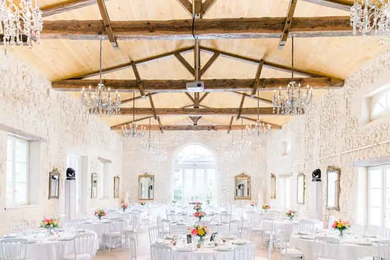 Reception hall with exposed beams, chandeliers and round tables set