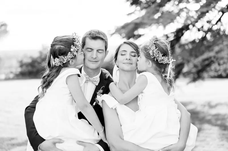 Two flower girls kissing the bride and groom on the cheek, black and white