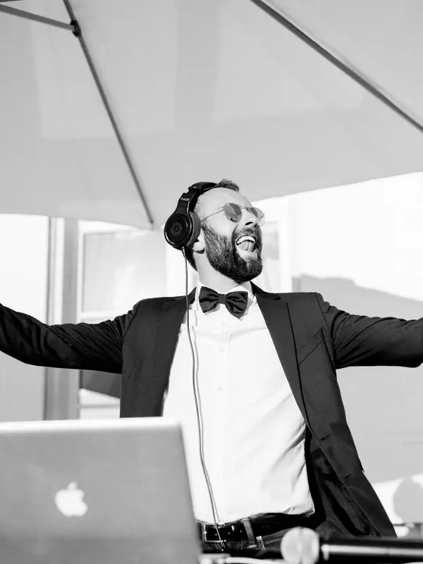 DJ in a bow tie with outstretched arms behind his decks, black and white