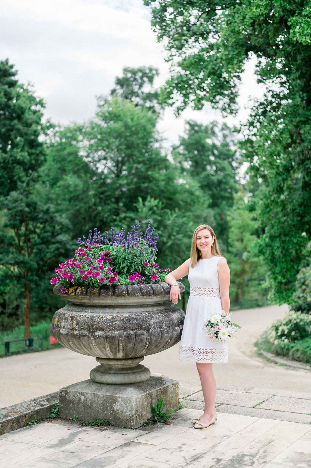 Tamara leaning on a flower-filled urn along a path in the Jardin Public