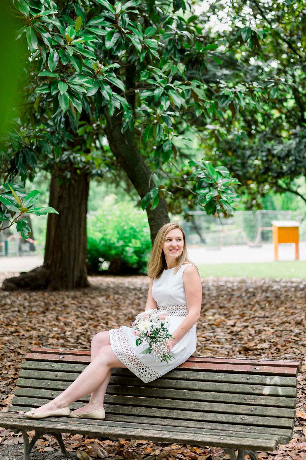 Tamara sitting on a bench beneath a magnolia, bouquet in hand