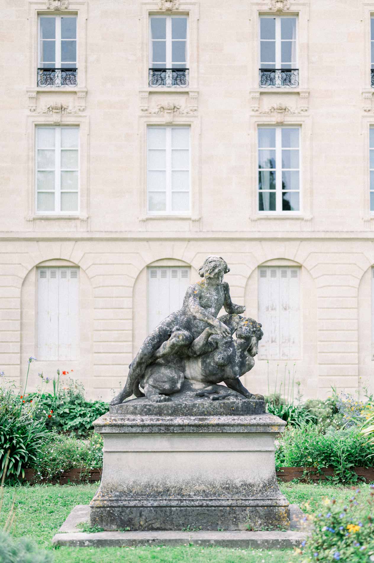 Stone statue of children before a classical façade beside the Jardin Public