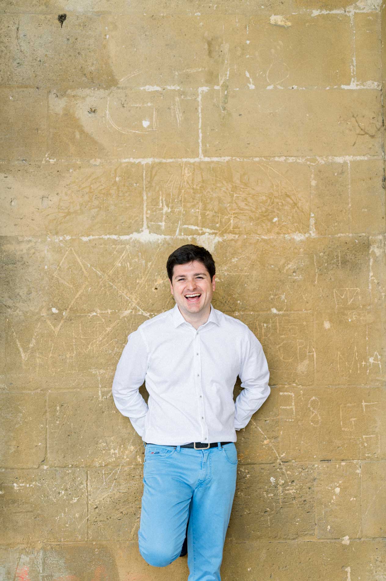 Nicolas laughing, leaning against a stone wall