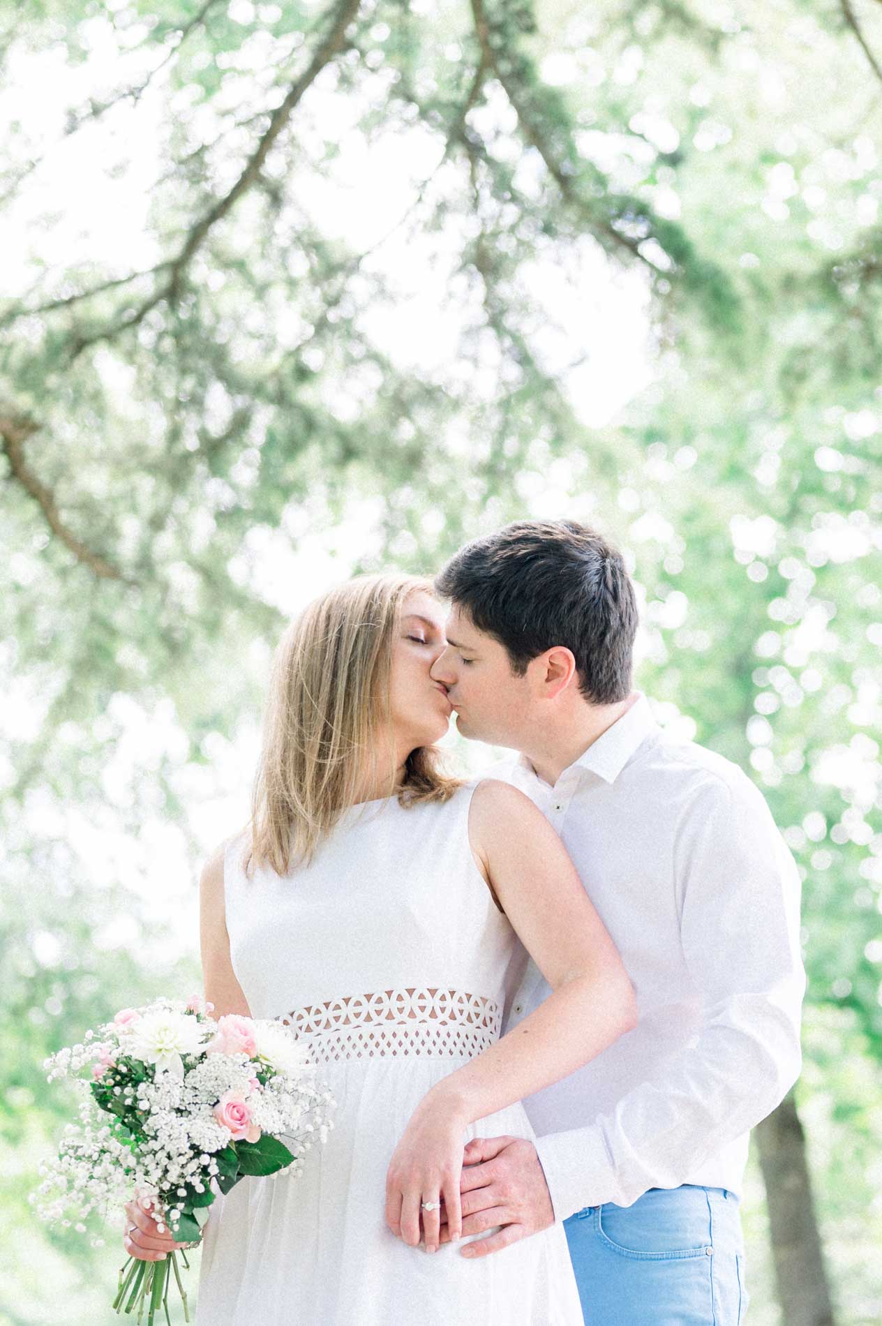 Tamara and Nicolas kissing beneath the trees, bouquet in hand