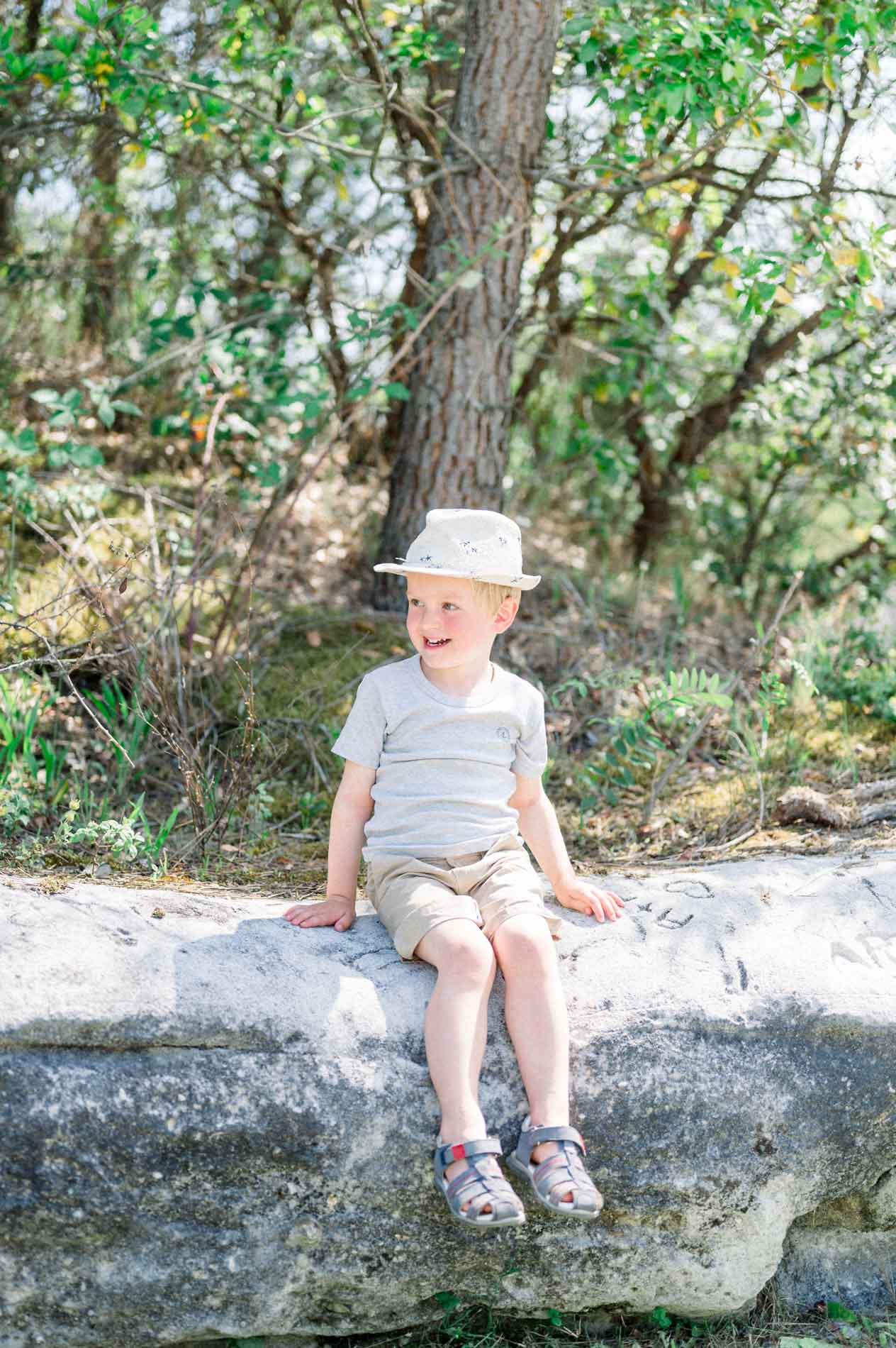 Little boy in a straw hat sitting on a rock beneath the trees