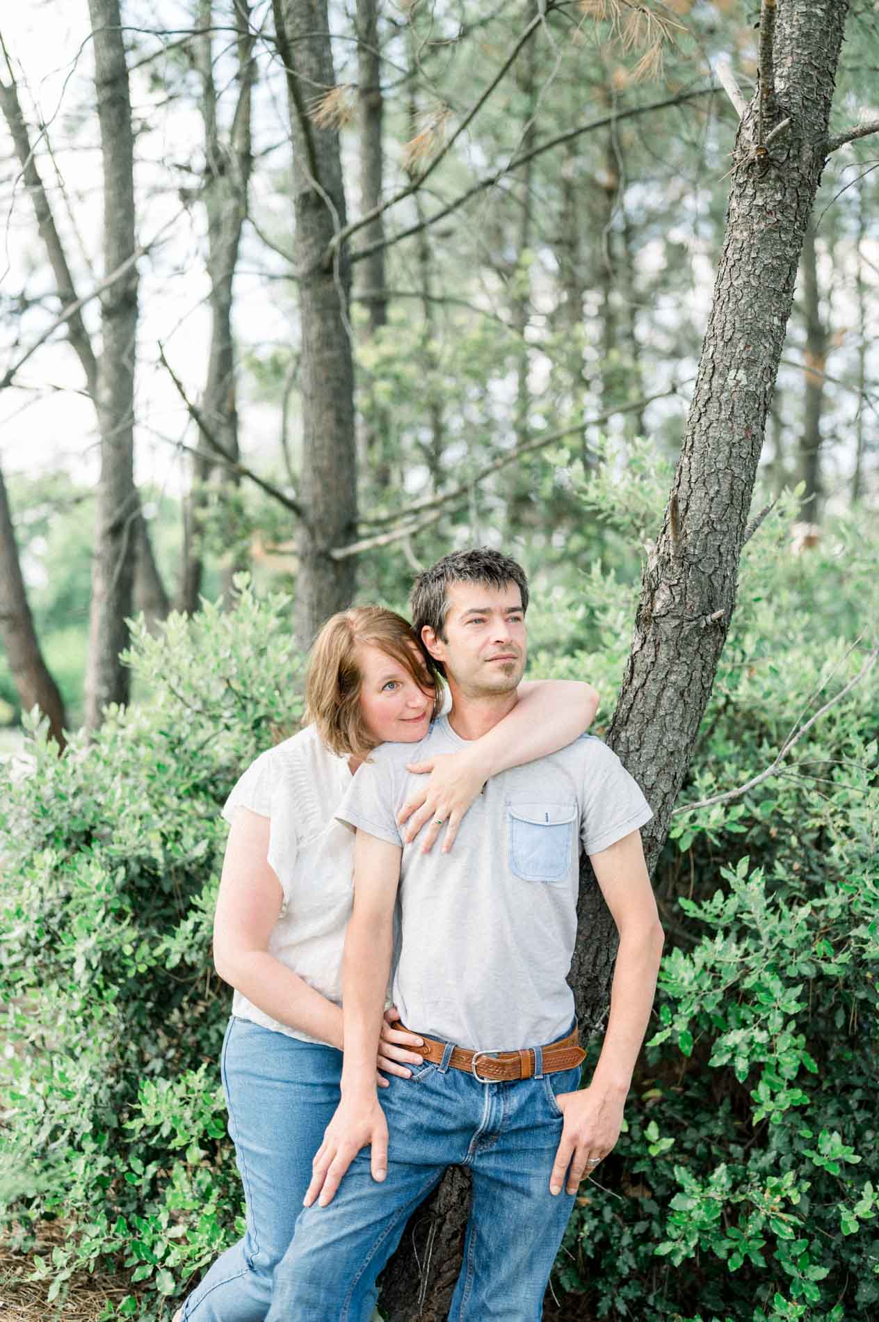 The parents embracing and smiling in front of a grove of pines