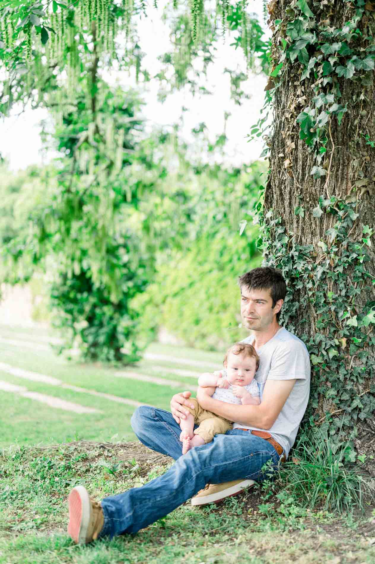 The dad sitting against a tree with his baby on his lap