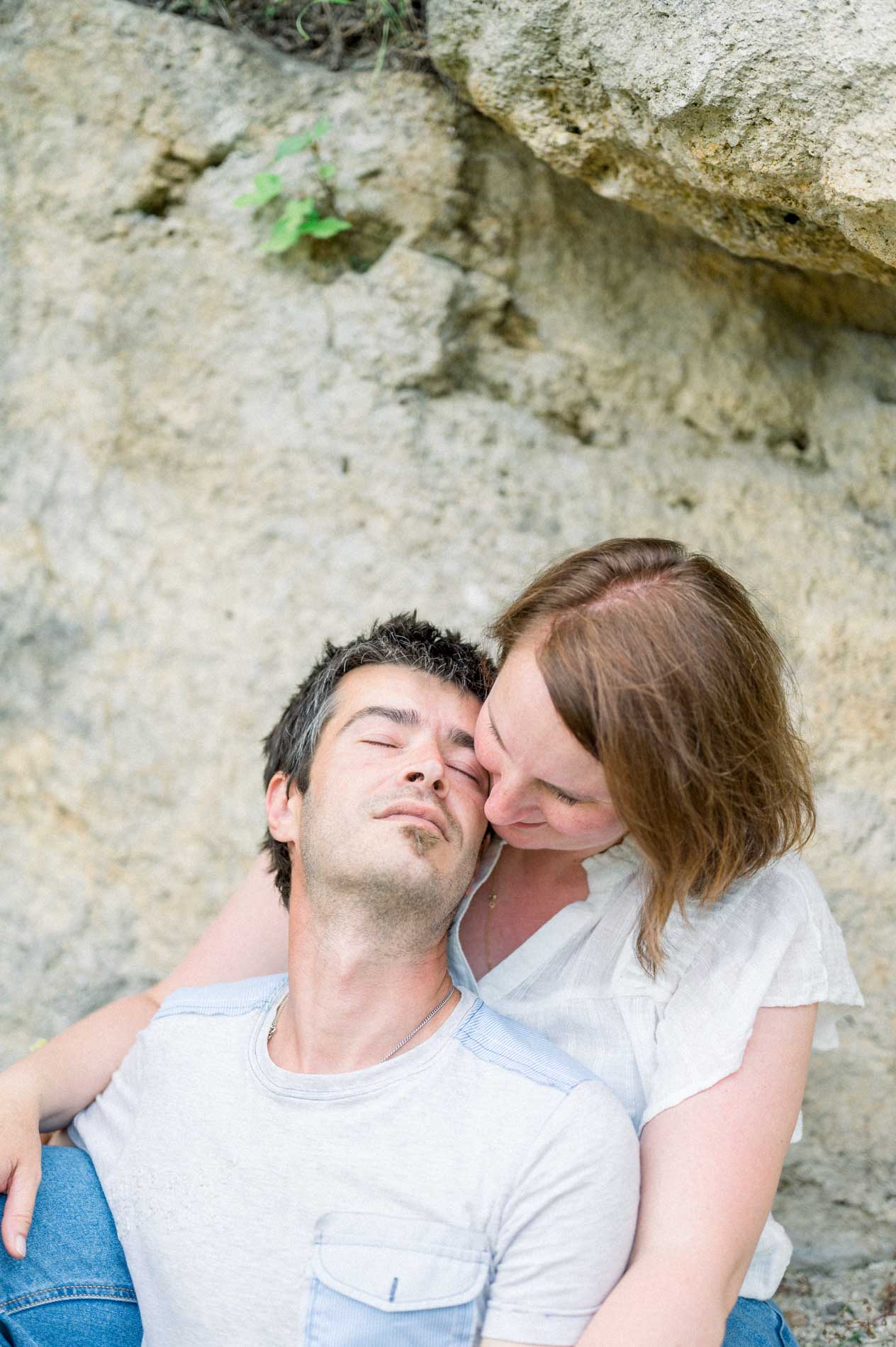 The mum kissing the dad's cheek as they lean against the rock