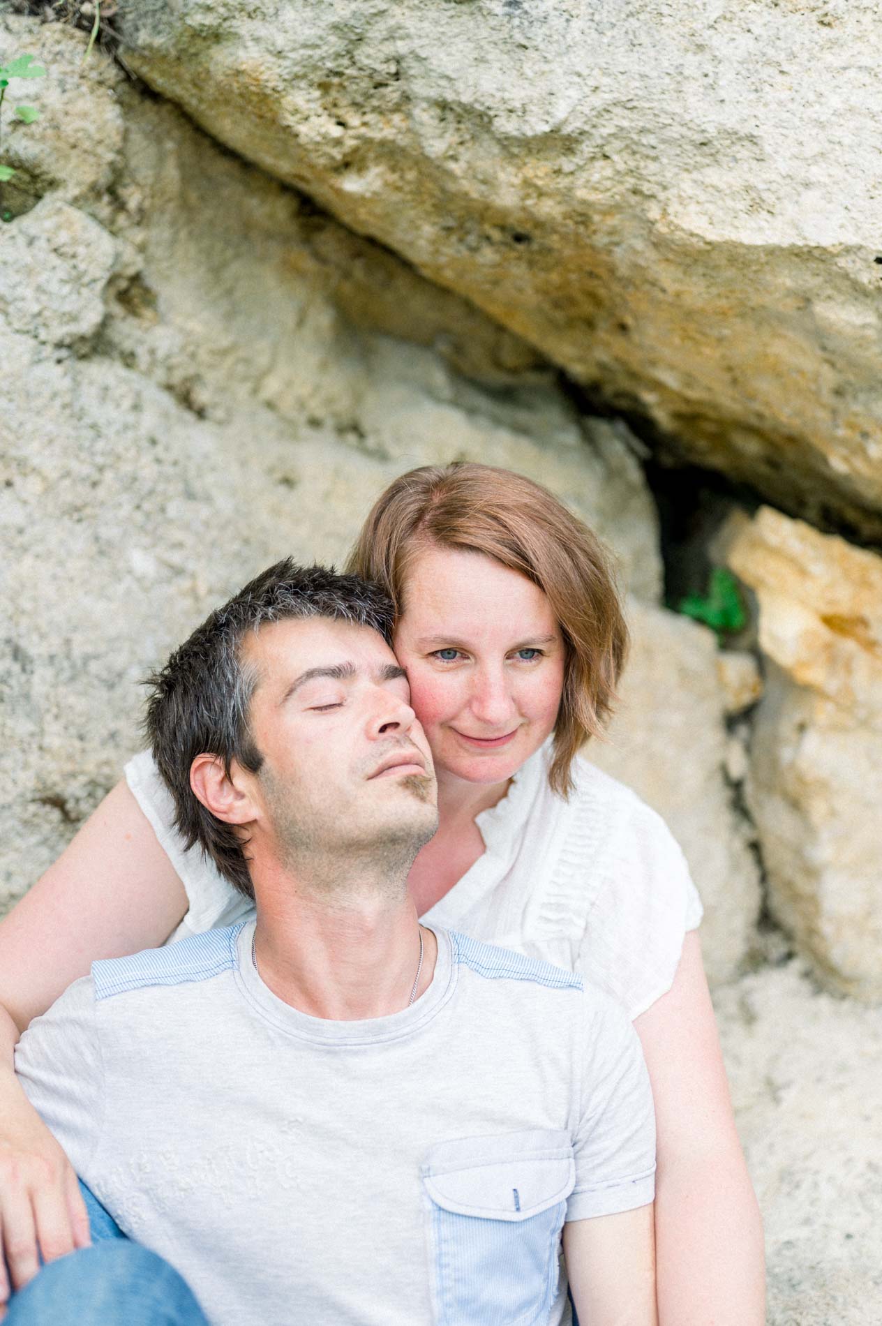 The smiling mum hugging the dad, his eyes closed, against the rock