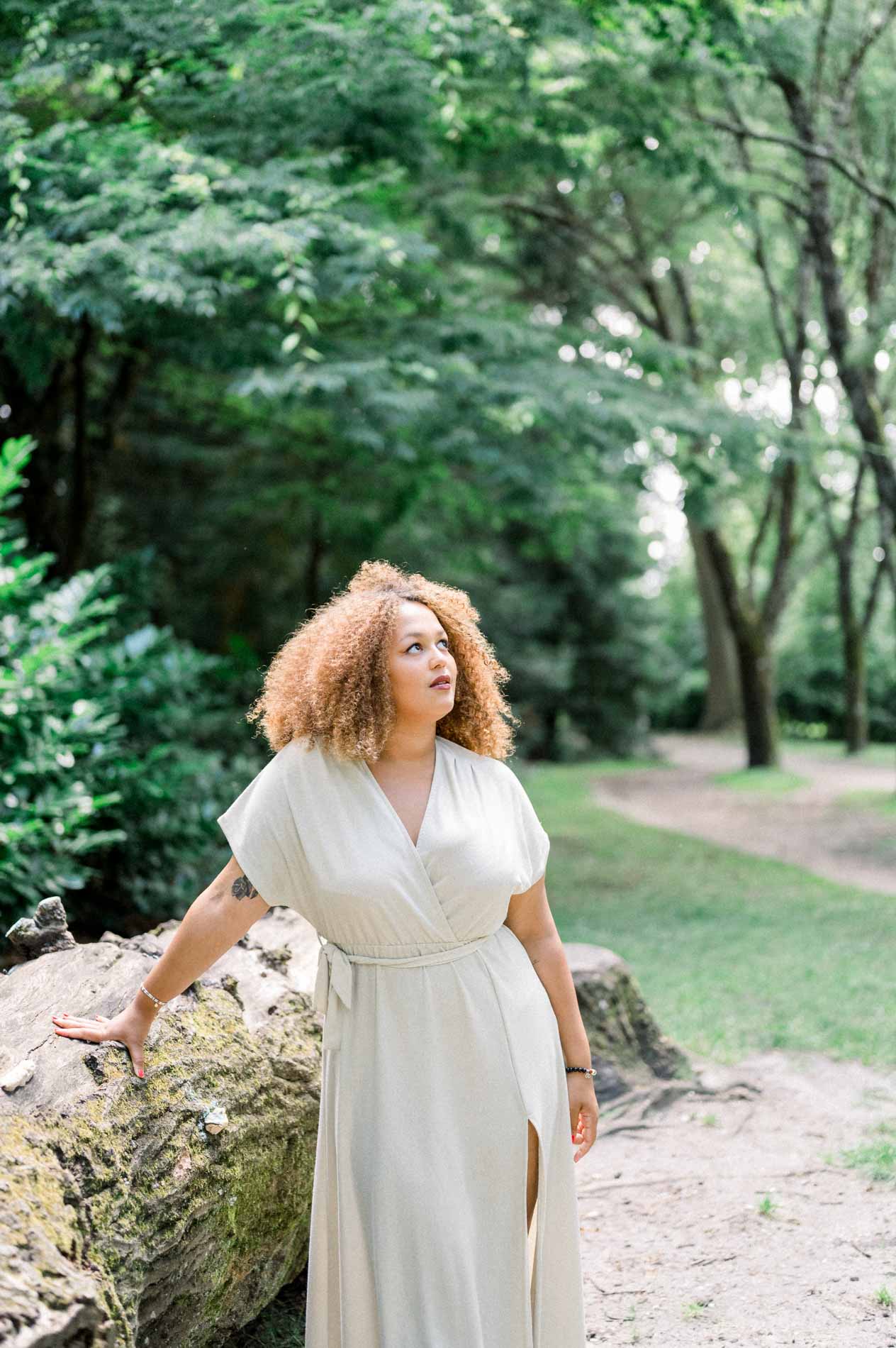 Young woman with curly hair in a cream dress leaning on a rock