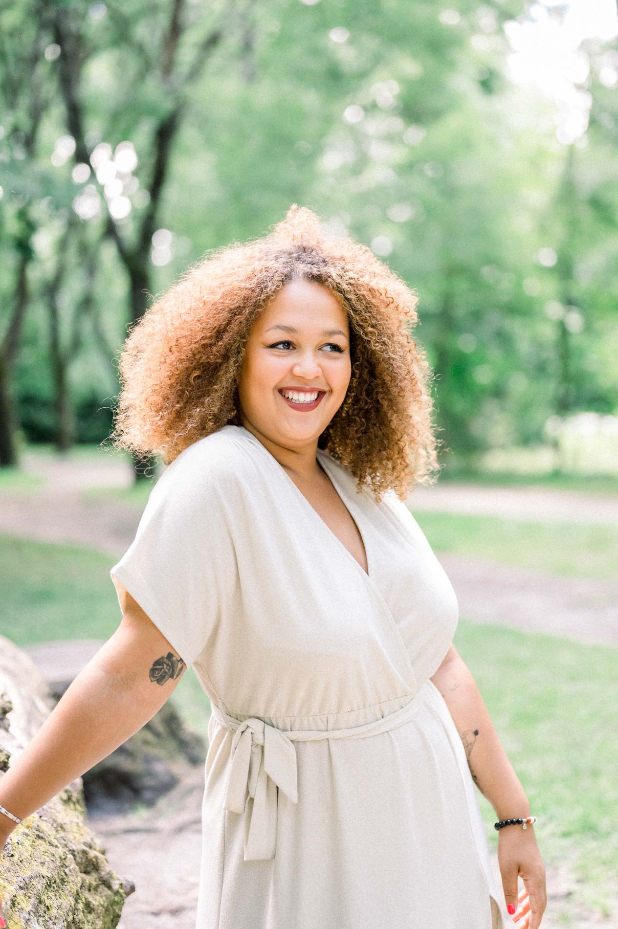 Smiling young woman in a cream wrap dress on a park path