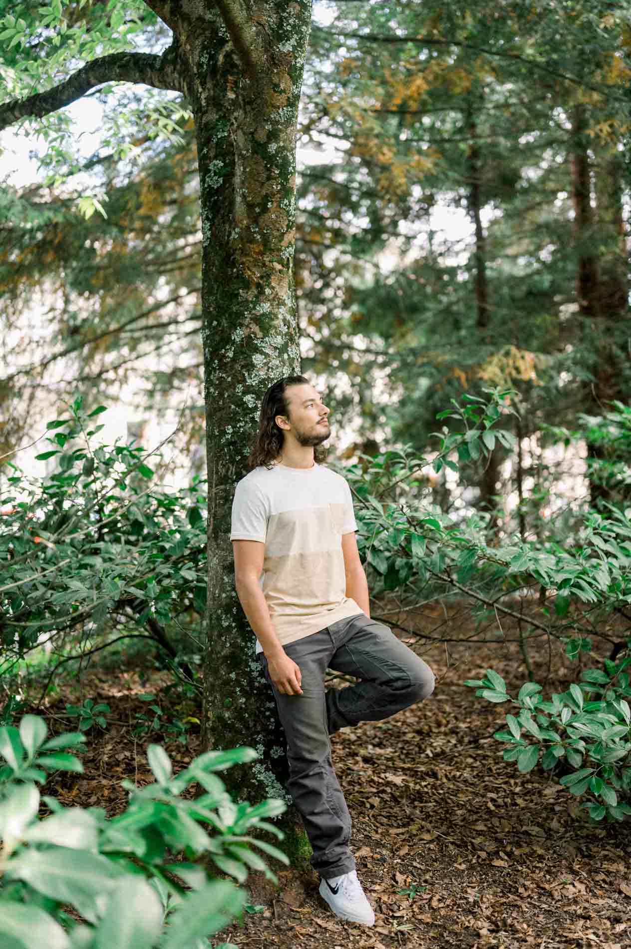 Young man leaning against a tree among rhododendrons