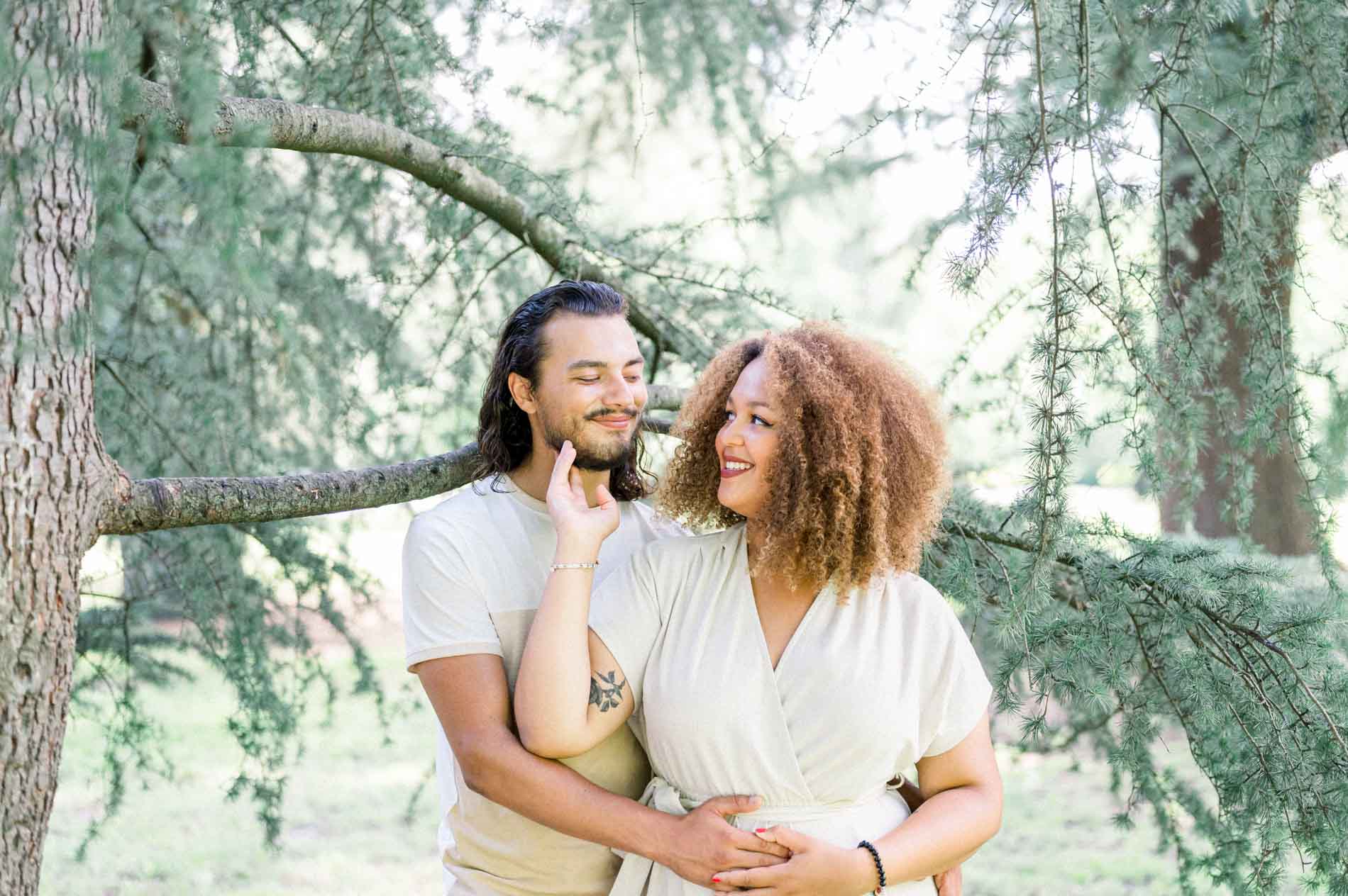 Couple embracing beneath a cedar branch, sharing a knowing look