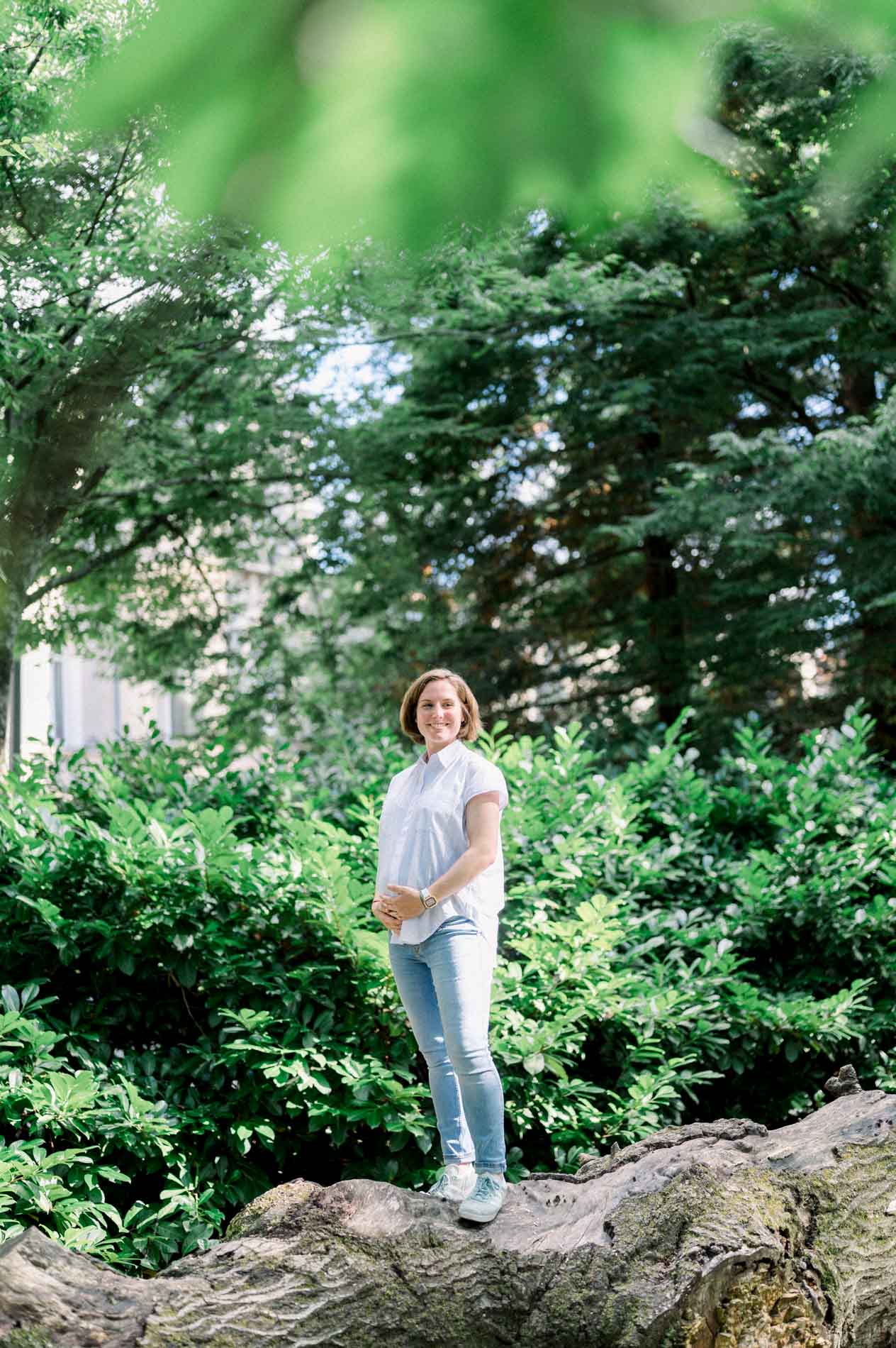 Mother-to-be standing on a fallen log amid the park's greenery