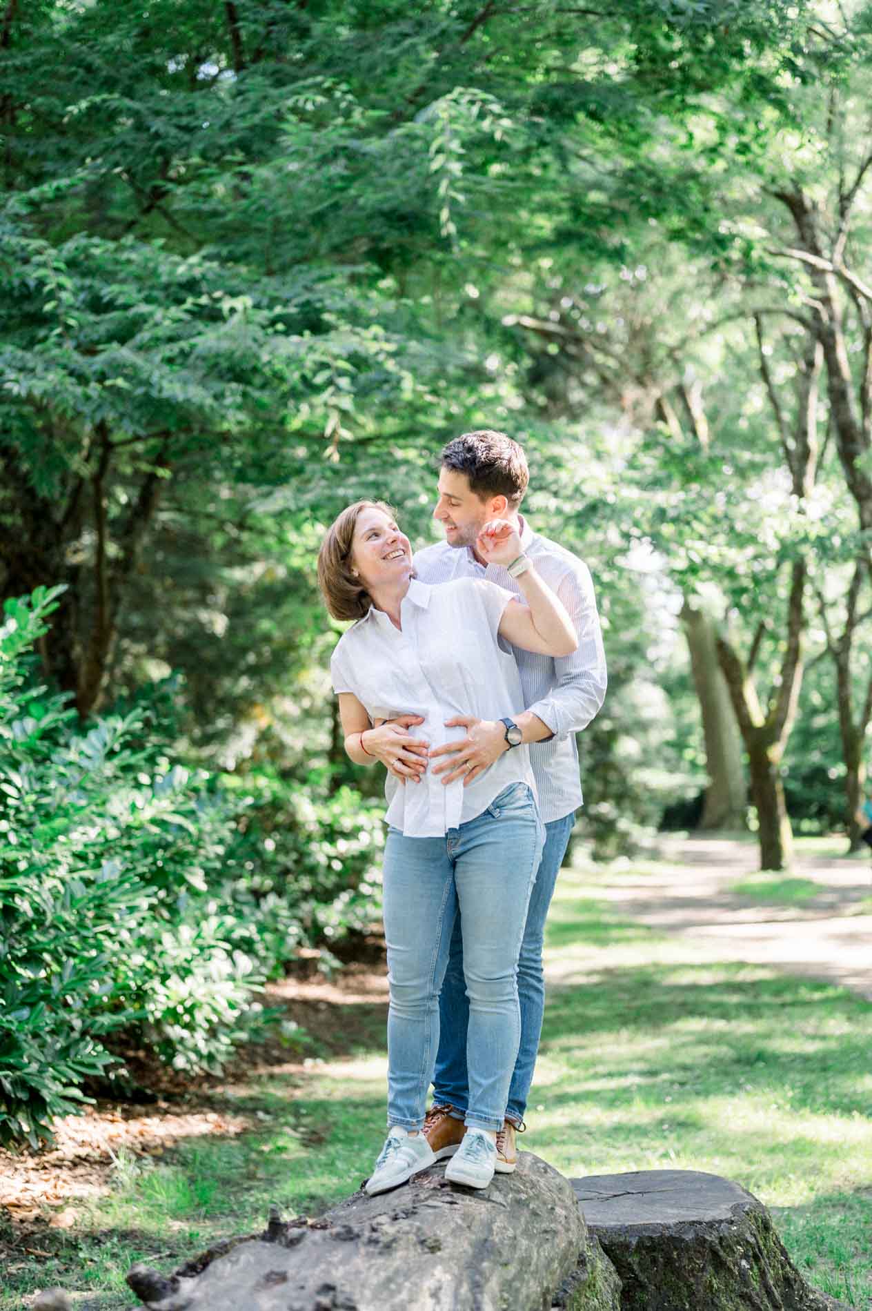 Couple embracing on a tree trunk, hands resting on the baby bump