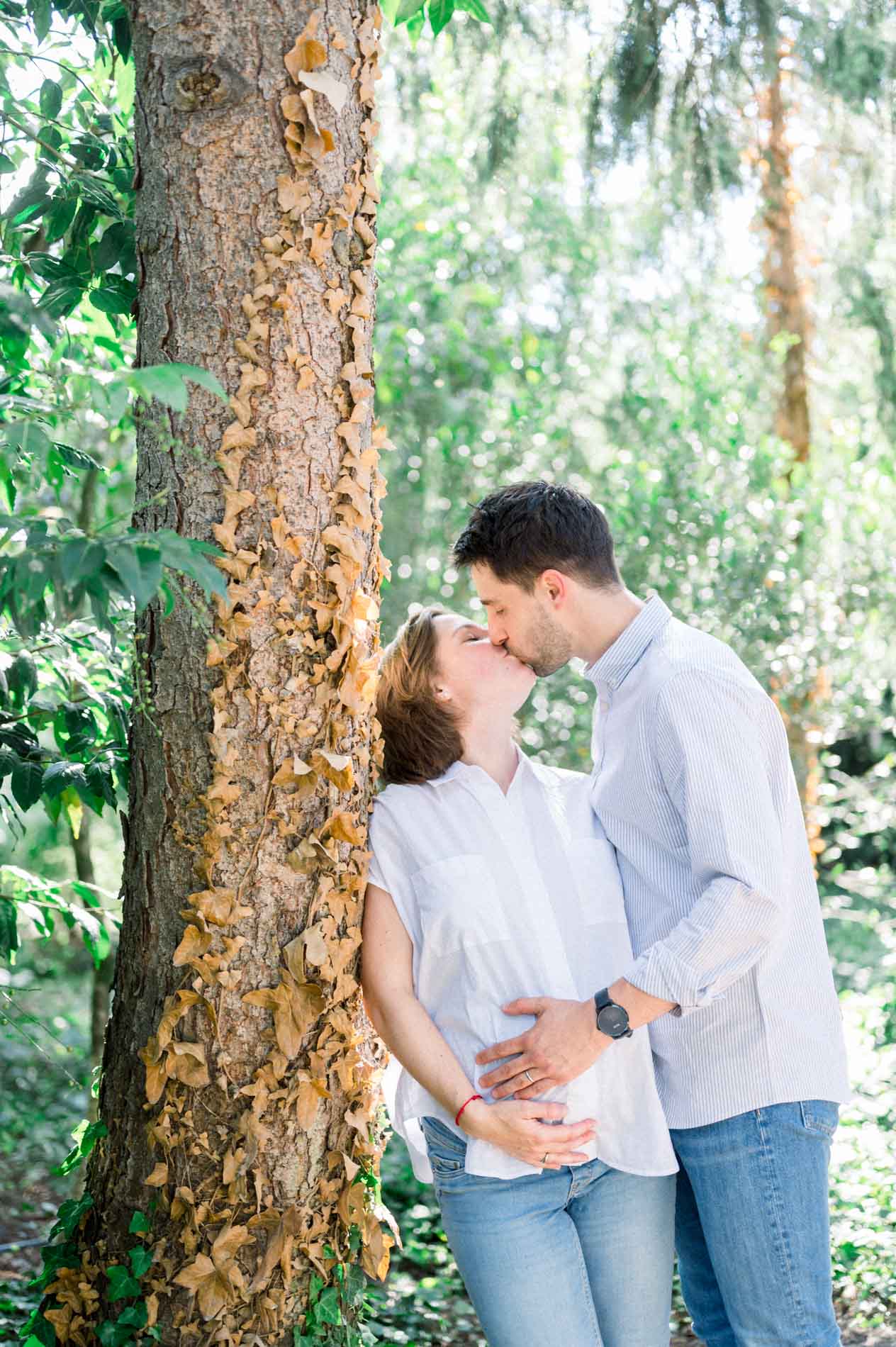 Couple kissing against a tree, hands on the pregnancy bump