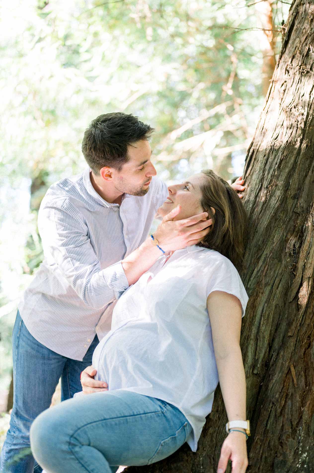 Father-to-be stroking his pregnant partner's face against a tree