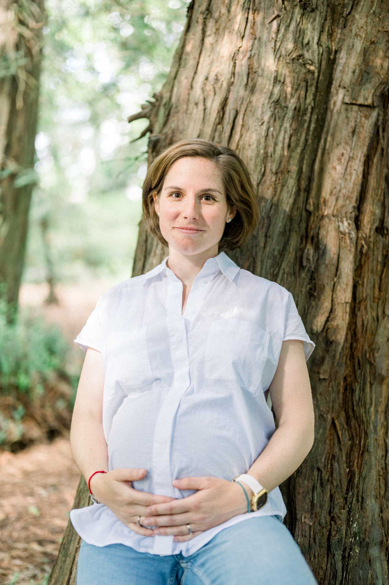 Pregnancy portrait of a woman seated against a tree trunk