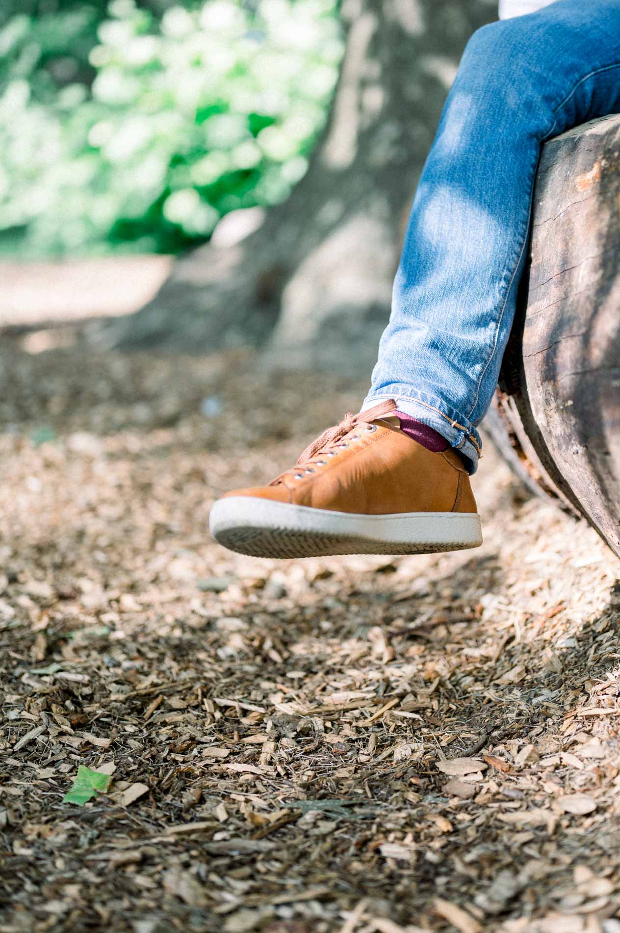 Detail of the father-to-be's trainers and jeans as he sits on a log