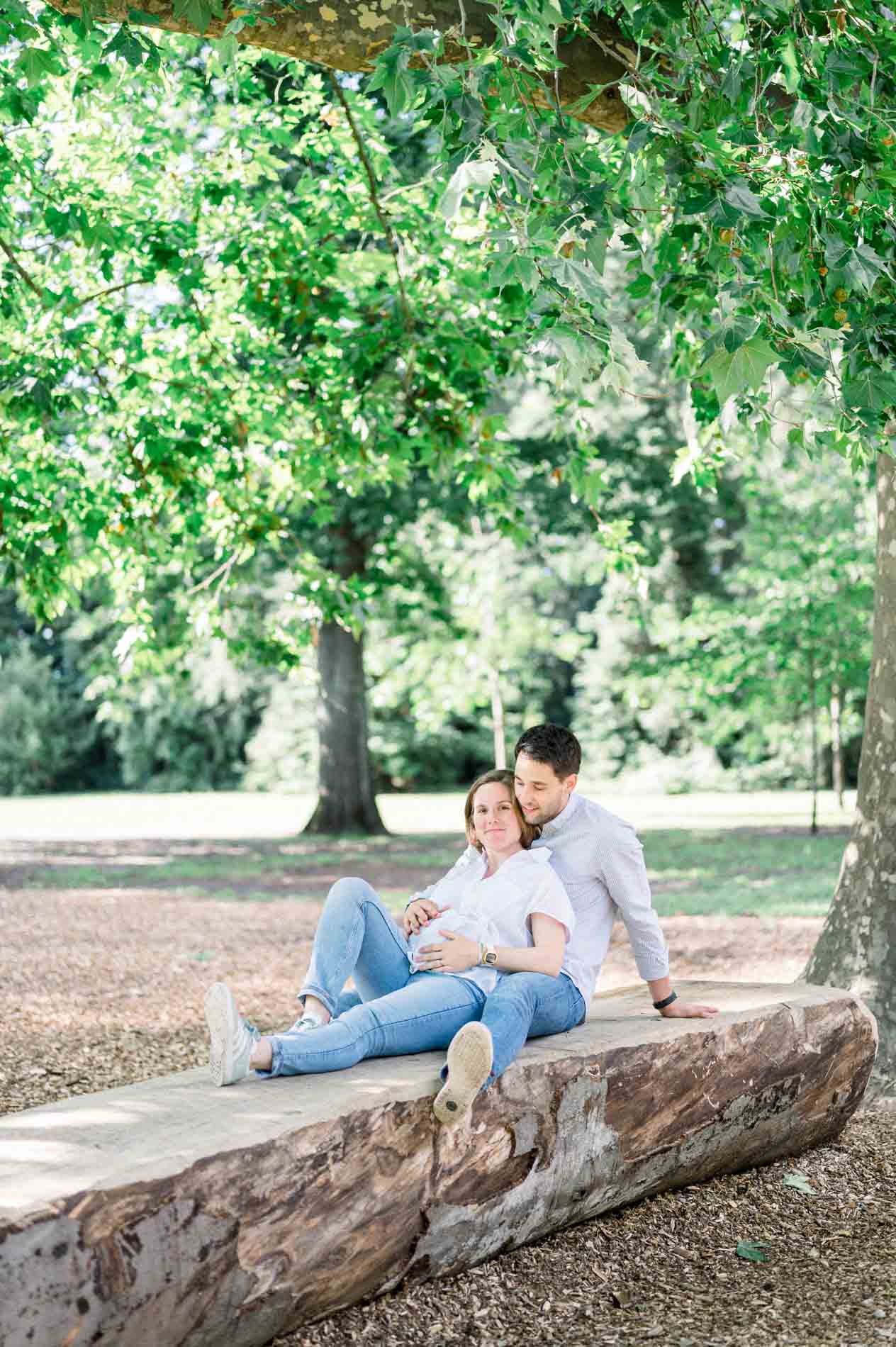 Couple sitting on a fallen log in the shade of the park trees