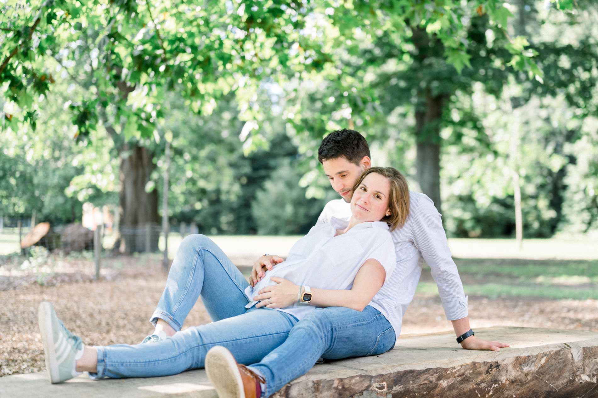 Parents-to-be lying back on a tree trunk in the park