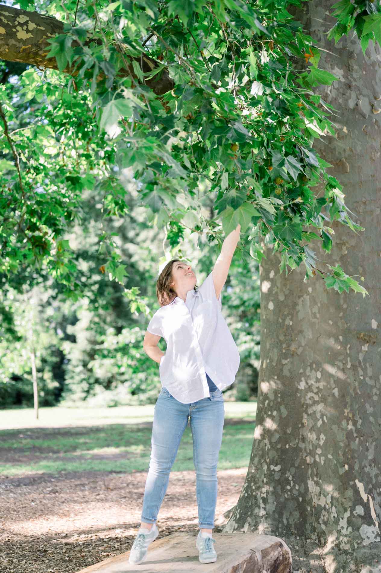 Mother-to-be reaching up towards the leaves of a large plane tree