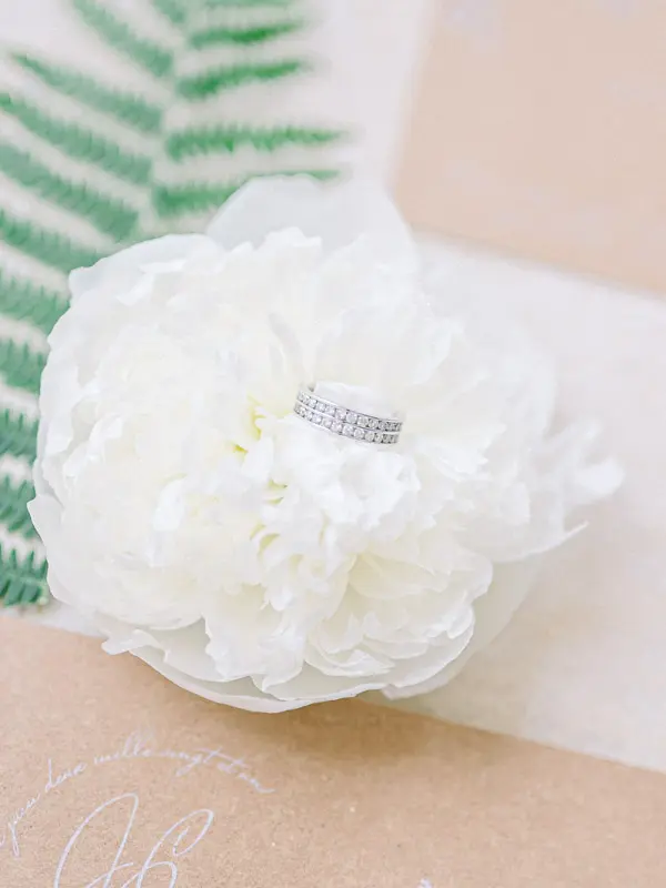 Wedding ring resting on a white peony beside a fern leaf