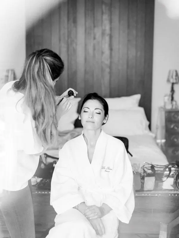 The bride in her robe having her makeup done, in black and white