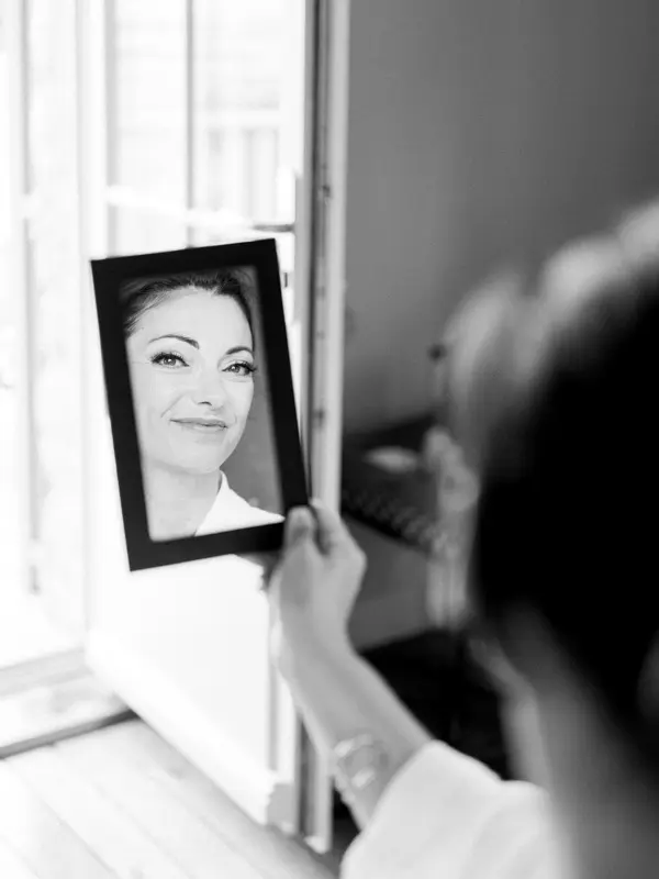 The bride looking at her reflection in a small hand mirror by the window