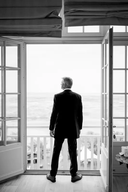 The groom seen from behind at an open window overlooking the bay, black and white