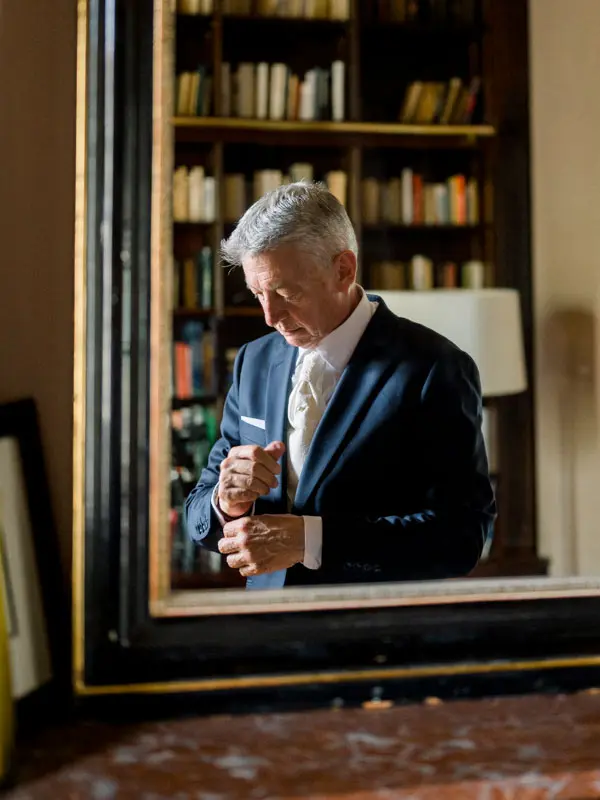 The groom adjusting his cuff in front of the library mirror