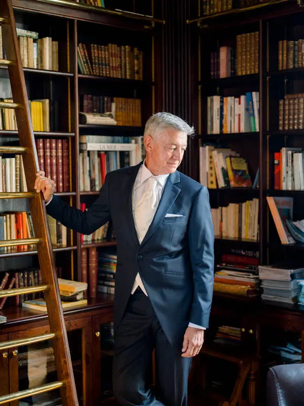 The groom in a blue suit posing in the villa's wood-panelled library
