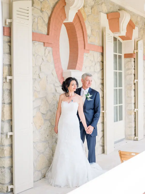 The bride and groom hand in hand against the villa's stone wall