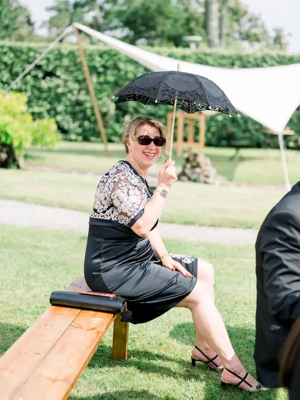 A guest with a black parasol seated on a bench during the ceremony
