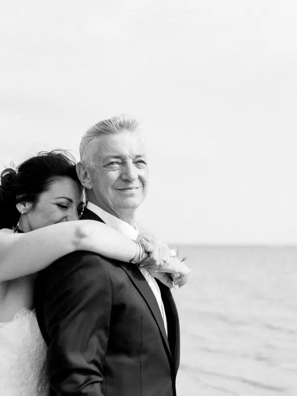 The bride hugging the groom from behind by the bay, in black and white